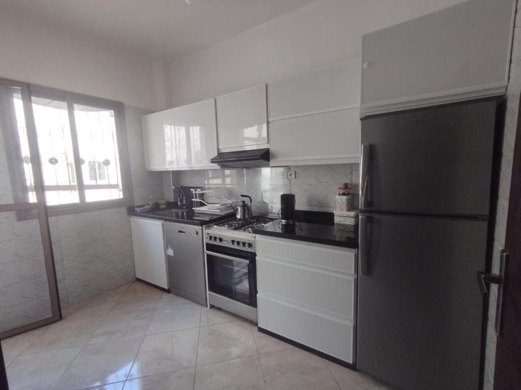 a kitchen with white cabinets and a stainless steel refrigerator at Appartement Cozy Louizia in Ben Yakhlef