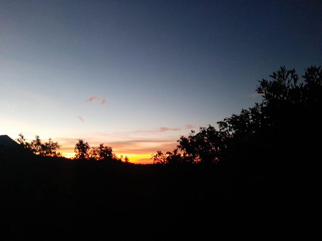 een zonsondergang boven een heuvel met bomen op de voorgrond bij CASA JARDIN in Sonsonate