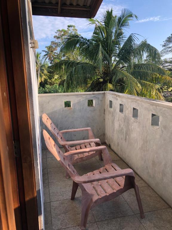 a pair of chairs on a balcony with a palm tree at senarathna guest house in Weligama