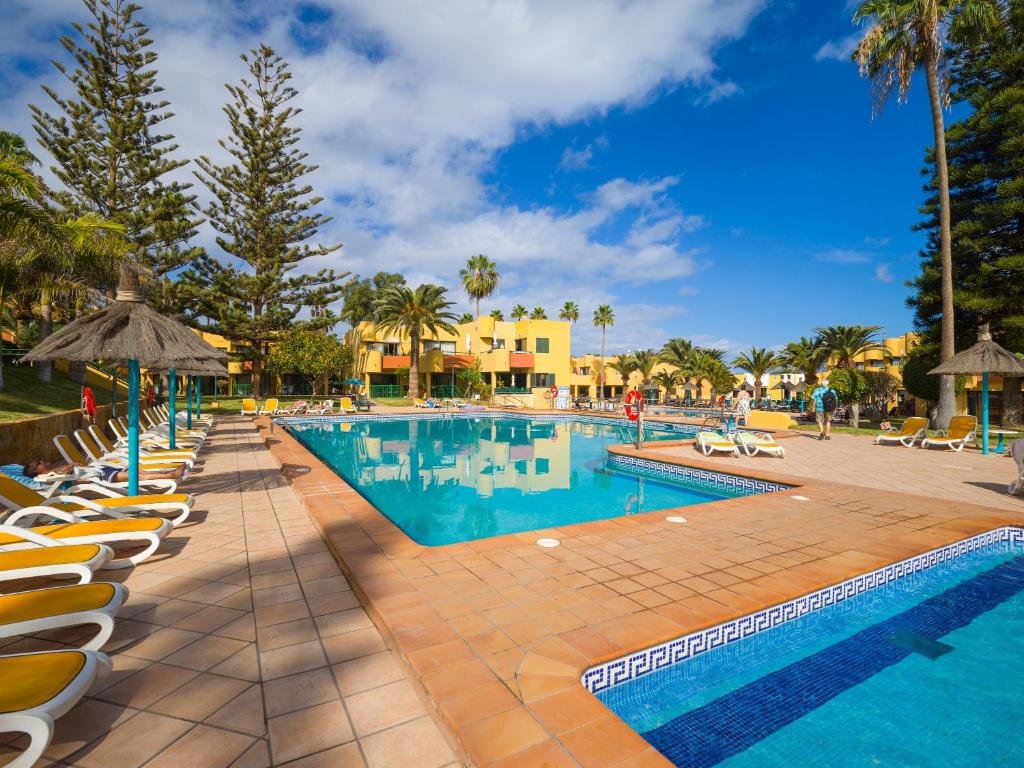 a resort pool with lounge chairs and palm trees at Casa Tindaya - 5 min walk from the Sea in Corralejo