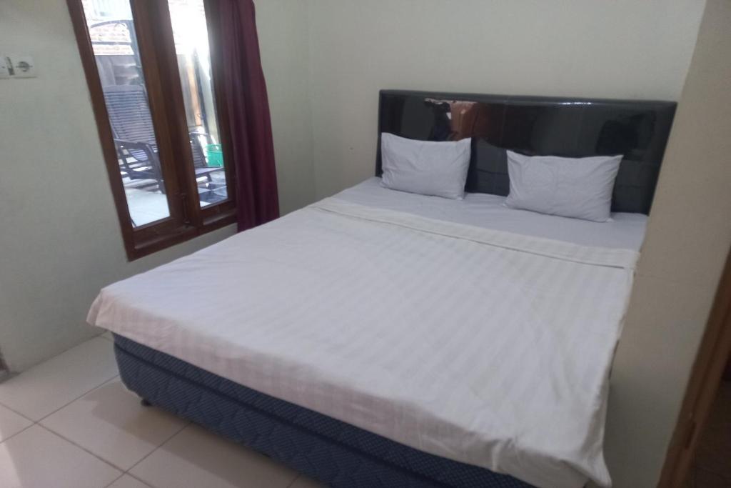 un letto con lenzuola e cuscini bianchi accanto a una finestra di SPOT ON 93557 Juan Kostel 2 a Purwokerto