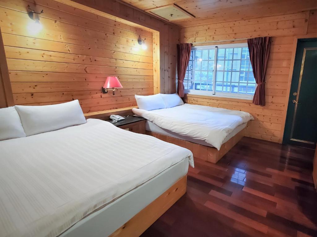 two beds in a room with wooden walls and a window at Kingtaiwan Hotel in Lugu Lake