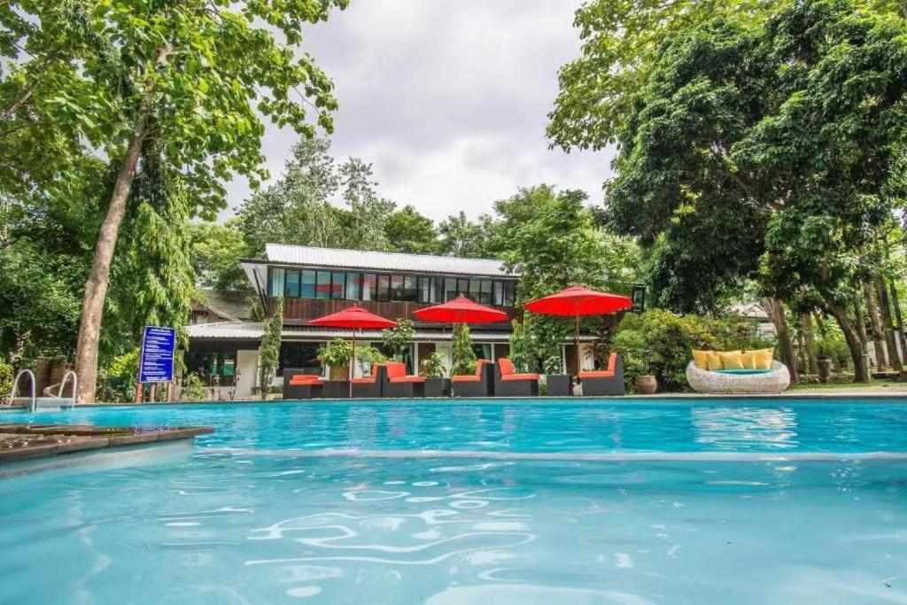 a swimming pool with chairs and red umbrellas at E-Outfitting Doikham Resort in Chiang Mai