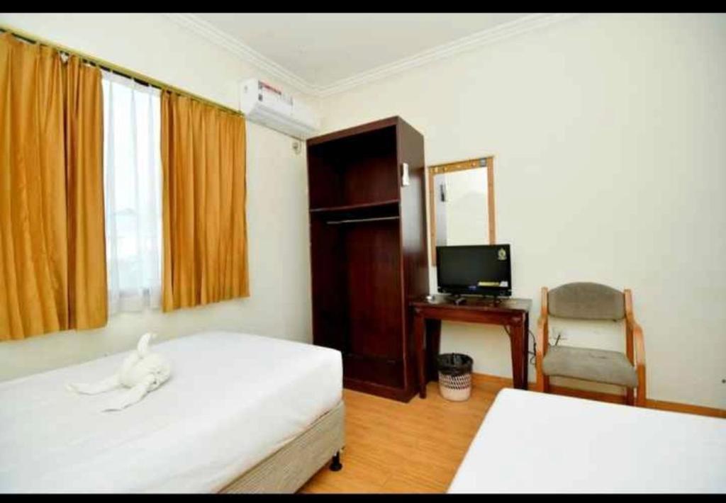 1 dormitorio con 2 camas, TV y silla en YUTA HOTEL, en Manado