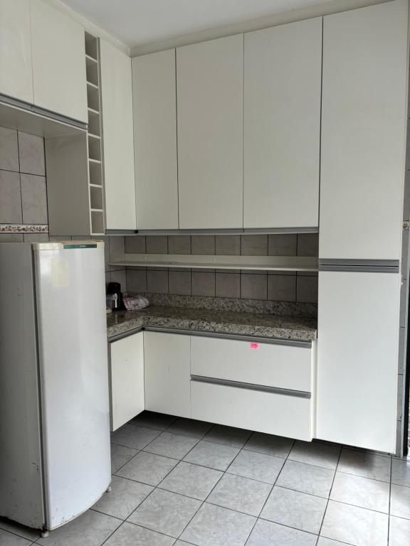 uma cozinha branca com armários brancos e um frigorífico em Hostel do mineiro em São José dos Campos