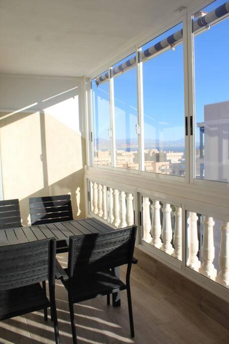 d'un balcon avec une table en bois, des chaises et des fenêtres. dans l'établissement Apartamento en Los Arenales, à Alicante