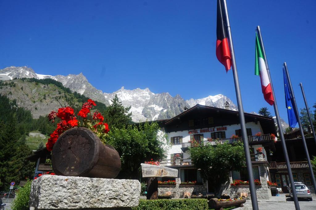 a building with flags in front of it with mountains at Hotel Aiguille Noire in Courmayeur