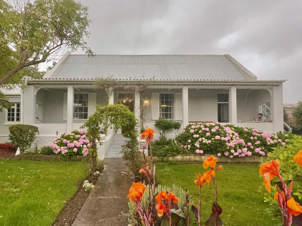 a white house with flowers in the yard at Rosehaven Cottage in Swellendam