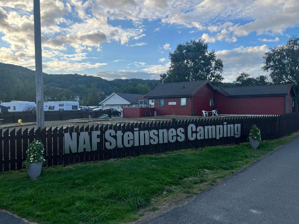 un cartel en una cerca al lado de un granero rojo en NAF Steinsnes Camping en Egersund