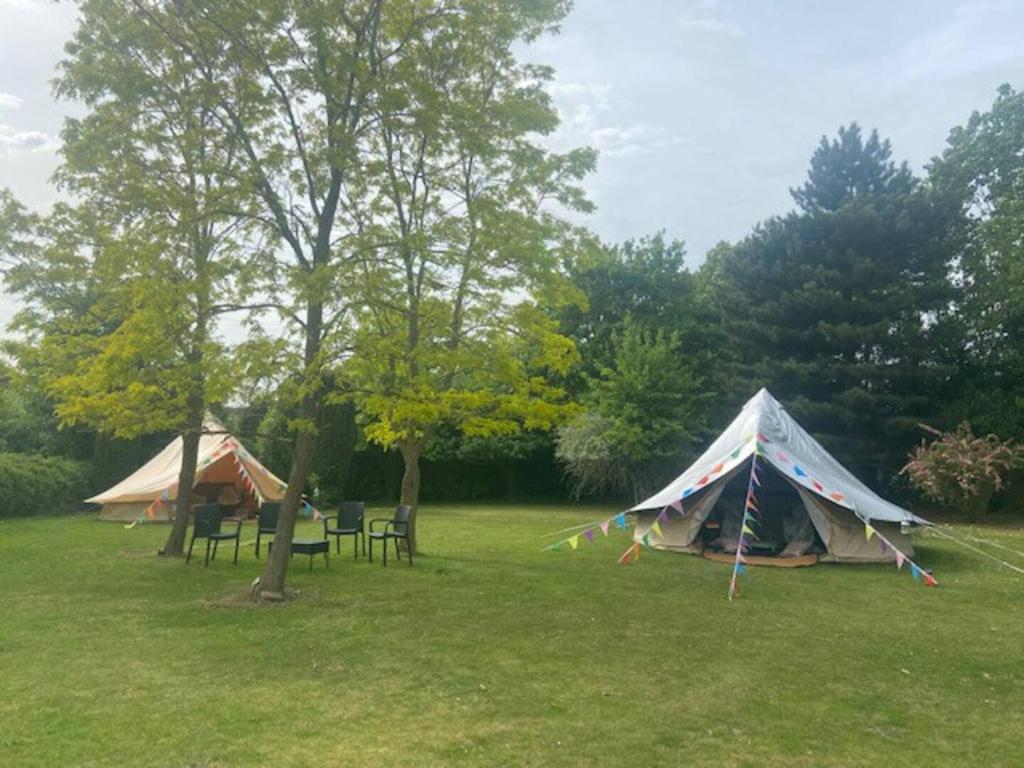 two tents in a field with tables and chairs at The Peacock Nest - Bell Tent in Sittingbourne