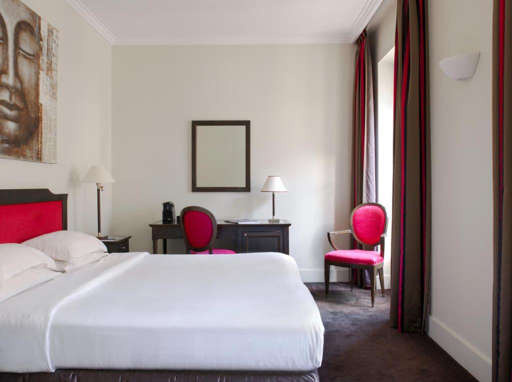 a bedroom with a white bed and two red chairs at Hotel Royal Saint Honore Paris Louvre in Paris