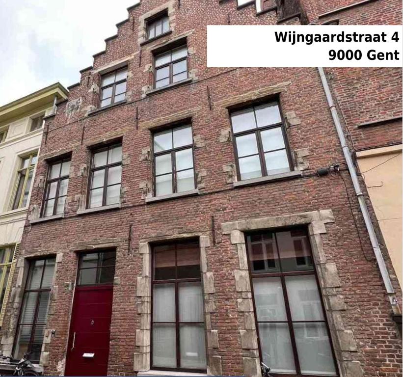 een bakstenen gebouw met ramen en een rode deur bij De Wijngaard in Gent