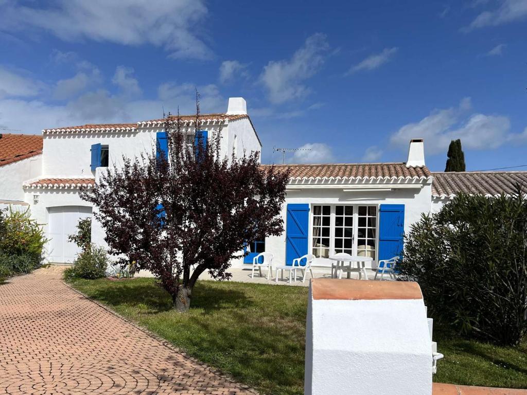une maison blanche avec des portes bleues et un arbre dans l'établissement Maison spacieuse 6 couchages, proche plage à La Guérinière, jardin clos, terrasse, calme - FR-1-224B-132, à La Guérinière