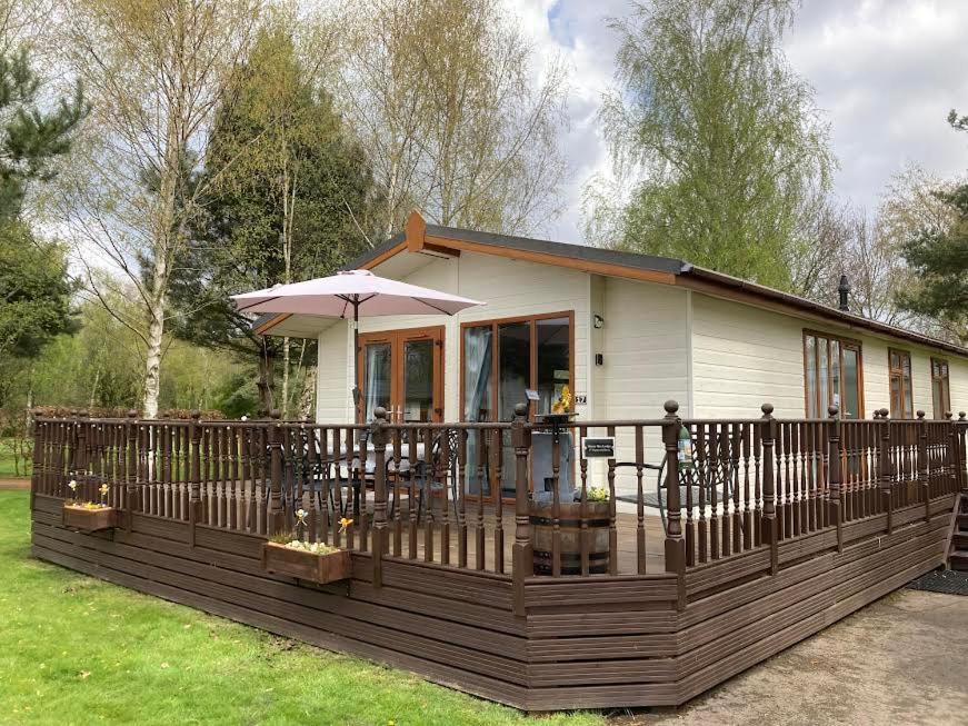 a small house with a deck with an umbrella at Honeybee Lodge in Wisbech