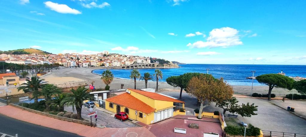a view of a beach with a yellow house and the ocean at Appartement VUE MER TERRASSE CLIM WIFI in Banyuls-sur-Mer