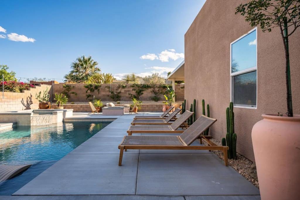 a row of benches sitting next to a swimming pool at Pueblo Viejo Desert Minimalist Pool Home in Bermuda Dunes