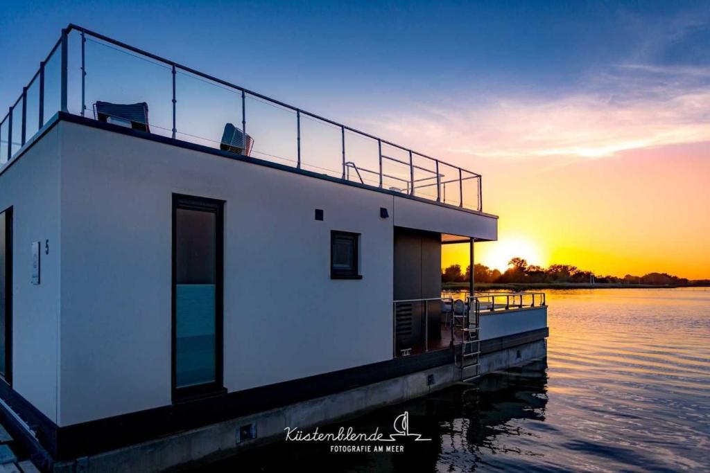 een huis op het water met de zonsondergang op de achtergrond bij Hausboot Boddenperle in Ribnitz-Damgarten