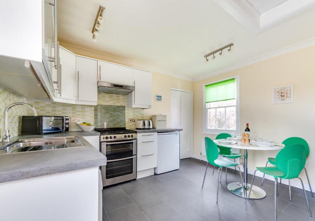 uma cozinha com armários brancos e uma mesa com cadeiras verdes em Alma Rise em Melton