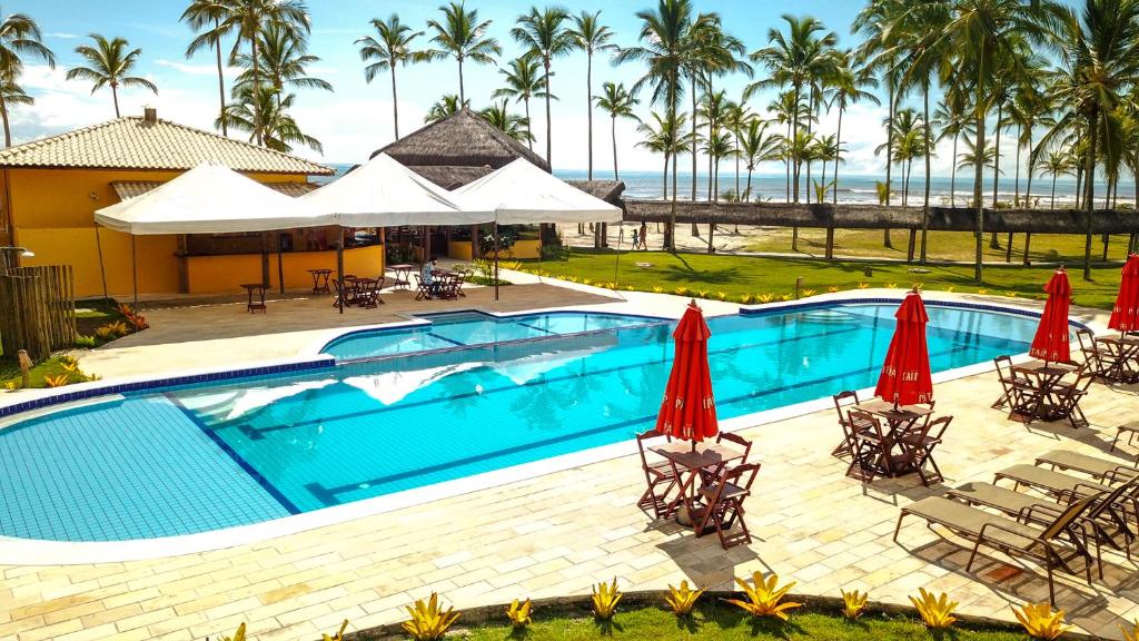 a swimming pool with chairs and umbrellas and the ocean at Makaira Beach Resort in Canavieiras