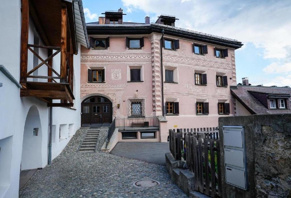 un edificio rosa con un cancello di fronte di Chesa Fischer Wohnung Palü ÖV-Inklusive a Samedan