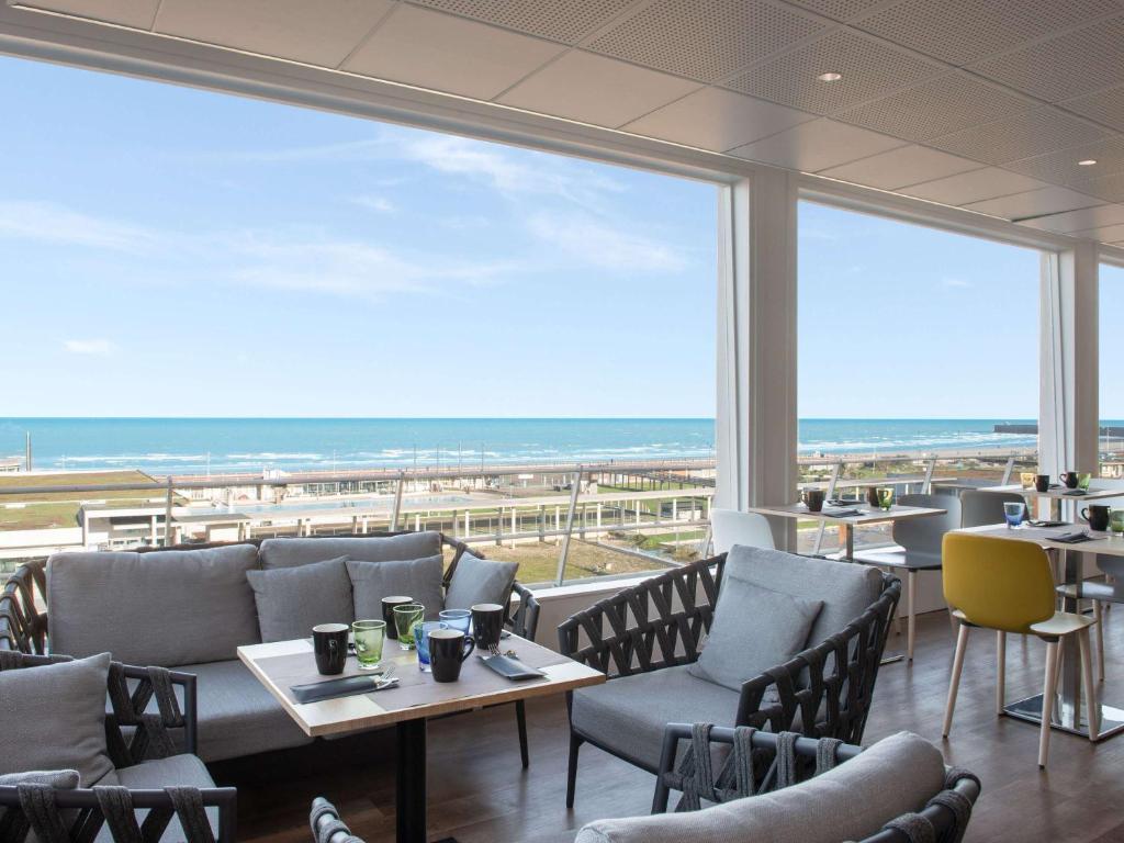 un restaurante con sillas y mesas y vistas al océano en Mercure Dieppe La Présidence en Dieppe
