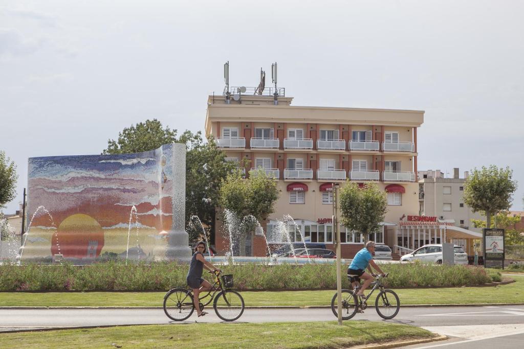 two people riding bikes in front of a building at Hotel Silvia in Empuriabrava