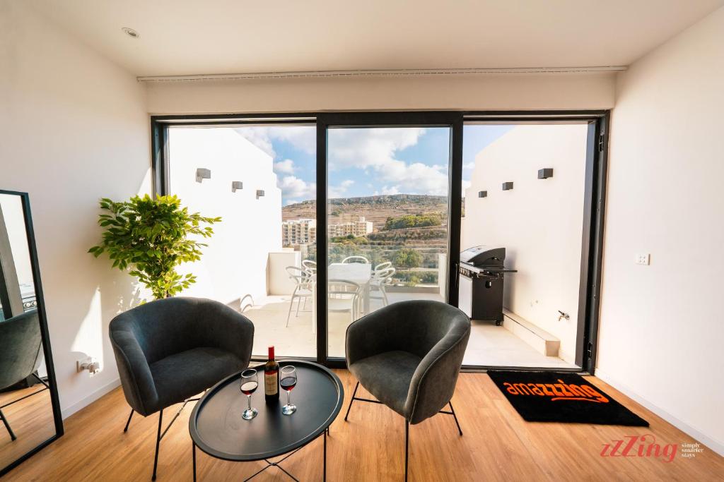 uma sala de estar com cadeiras, uma mesa e uma grande janela em A Stylishly Dreamy Gozo Apartment em Marsalforn