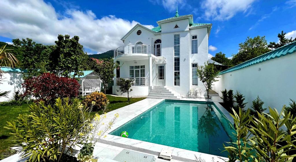 a white house with a swimming pool in front of it at Qafqaz Manor Kibana in Gabala