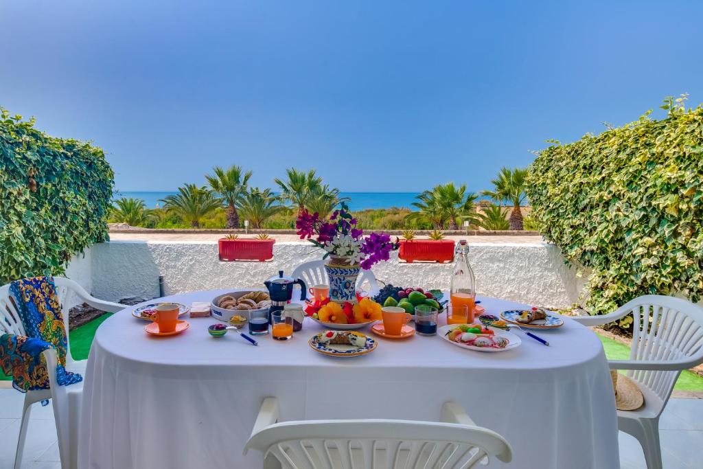 une table blanche avec de la nourriture sur elle avec l'océan en arrière-plan dans l'établissement Makauda Beach, à Sciacca