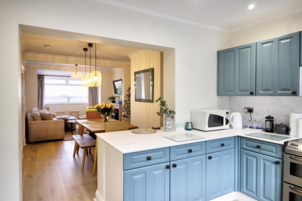 a kitchen with blue cabinets and a living room at Amazing sea views and hot tub in Amble