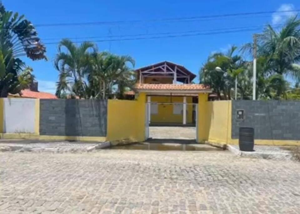 a yellow house with a fence and palm trees at Chácara in Estância