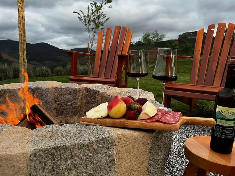 a plate of fruit and a glass of wine next to a fire pit at Cabana em Domingos Martins in Domingos Martins