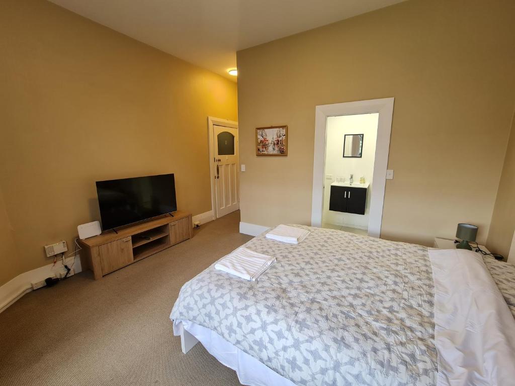 a bedroom with a bed and a flat screen tv at Dunedin City Centre Apartment Room B in Dunedin