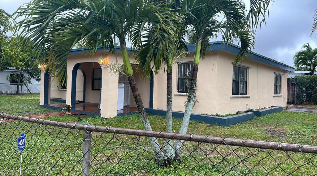 a house with two palm trees in front of a fence at Hospedaje North Miami in North Miami