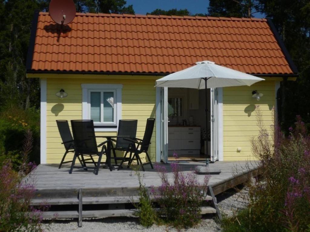 una pequeña casa amarilla con sillas y sombrilla en Kleines Ferienhaus - Tiny house - auf Gotland 700 Meter zum Meer en Ljugarn