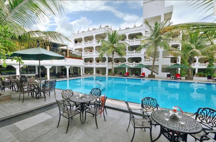 Sarkhej的住宿－Hotel Aarya Grand，游泳池旁的酒店设有桌椅