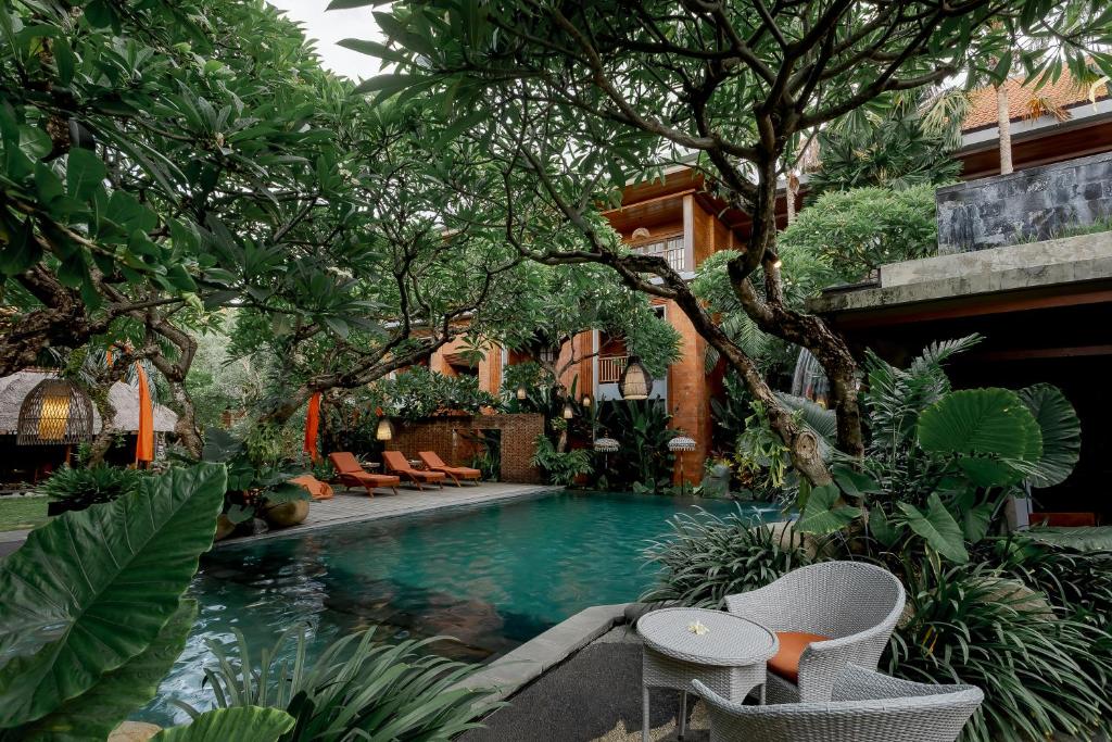 a swimming pool in a garden with chairs and trees at Fourteen Roses Boutique Hotel, Kuta in Legian
