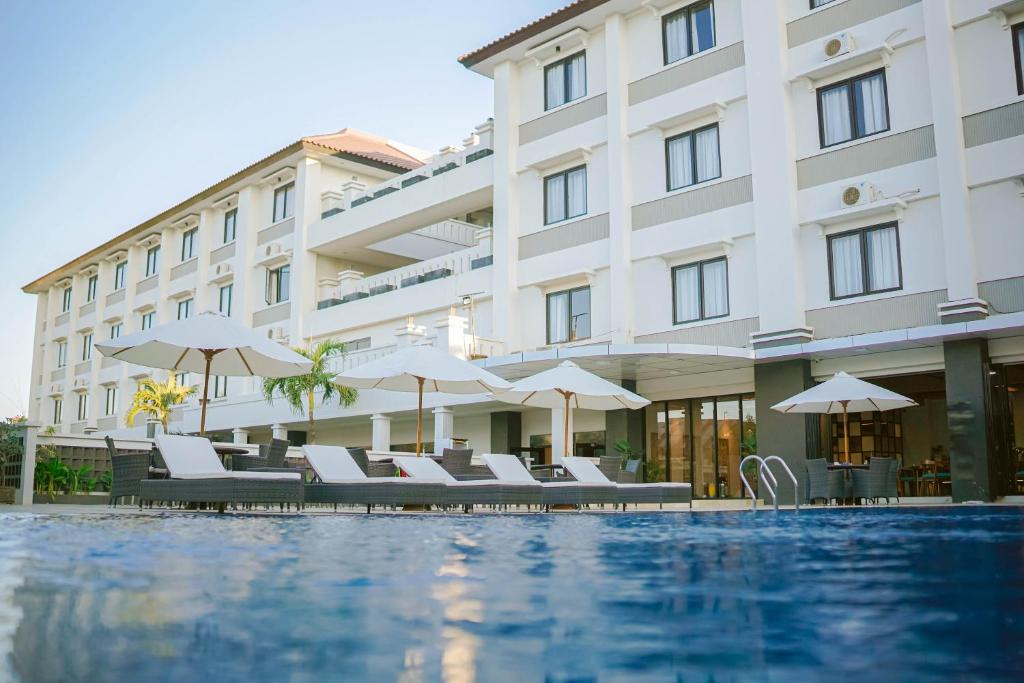 a hotel with a swimming pool with chairs and umbrellas at Sahid T-More Hotel in Kupang
