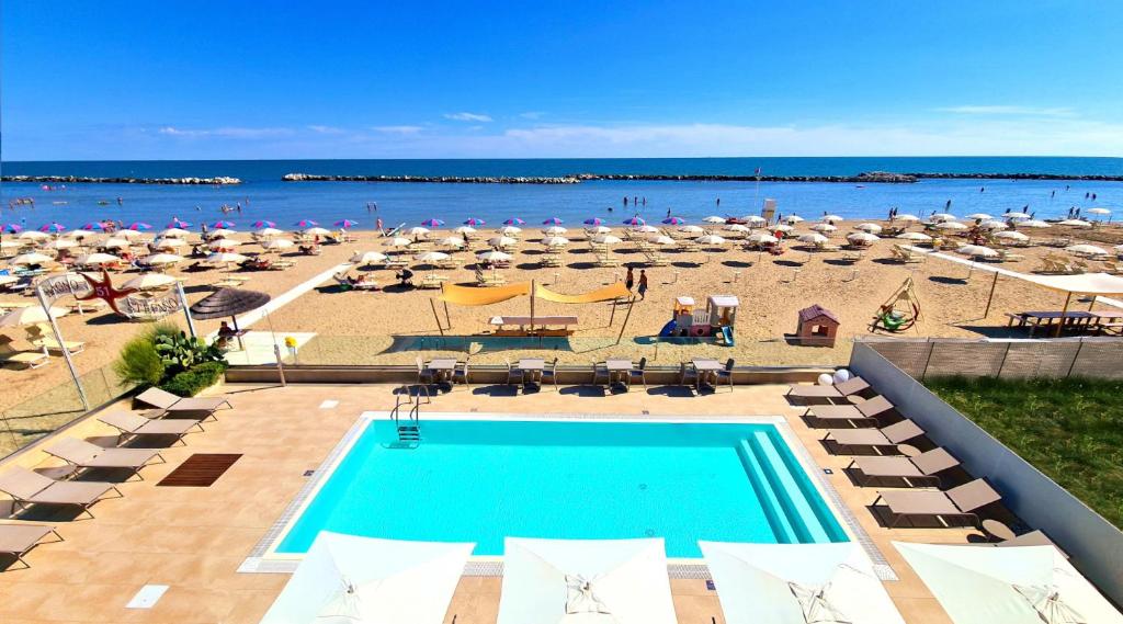 uma vista para uma praia com uma piscina e guarda-sóis em You & Me Beach Hotel em Rimini