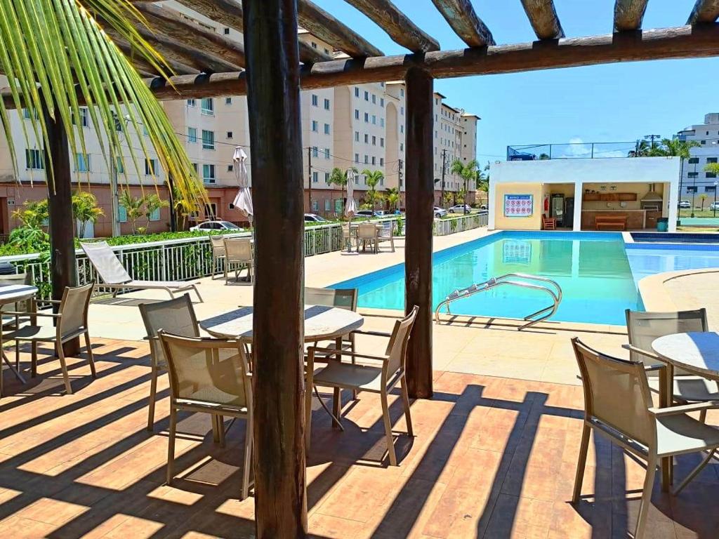 un patio avec des tables et des chaises à côté d'une piscine dans l'établissement Apartamento aconchegante em condomínio perto da praia, à Ilhéus