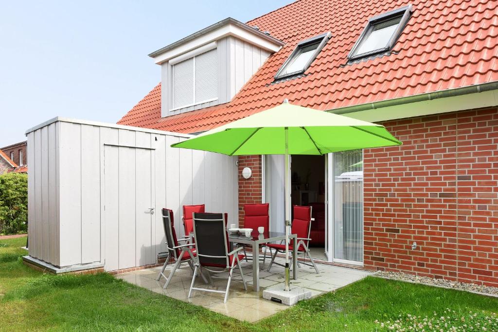 a table and chairs under a green umbrella on a patio at Ferienhaus Antares - Uns Huus an t Küst in Bensersiel