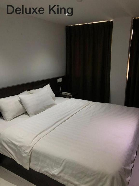een bed met witte lakens en kussens in een slaapkamer bij Hotel Vistana Micassa in Taiping