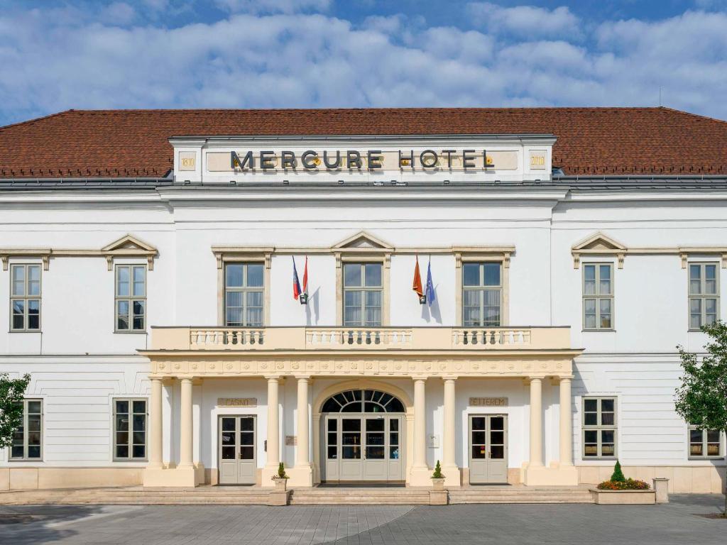 een groot wit gebouw met een bord voor het Mercure hotel bij Mercure Szekesfehervar Magyar Kiraly in Székesfehérvár