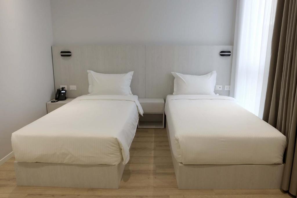two beds in a hotel room with white sheets at Metro Hotel Terminal in Tirana