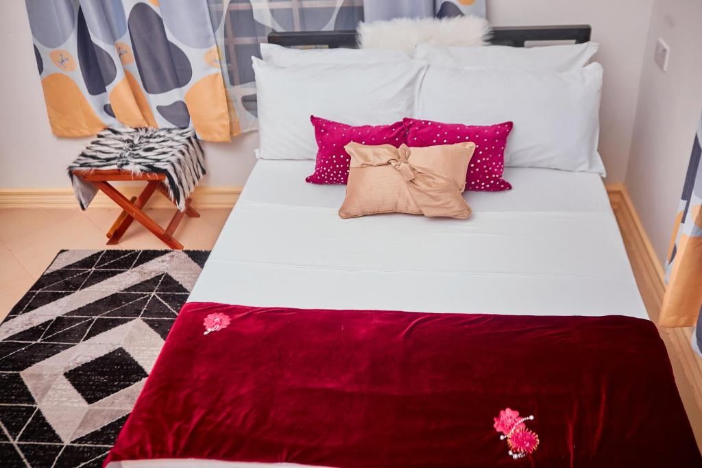 Una cama con almohadas rojas y blancas y una silla en Mama's Home Stay en Dodoma