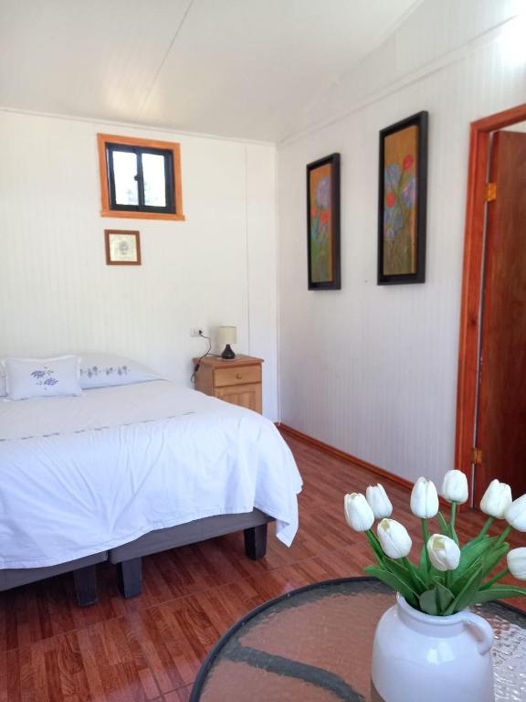 a bedroom with a bed and a vase with white flowers at Alojamiento Ximena in Coñaripe