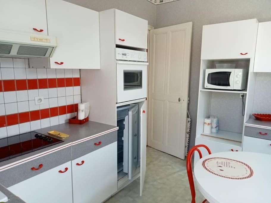 uma cozinha com armários brancos, uma mesa e um micro-ondas em F2 1ER ETAGE em Vigneulles-lès-Hattonchâtel