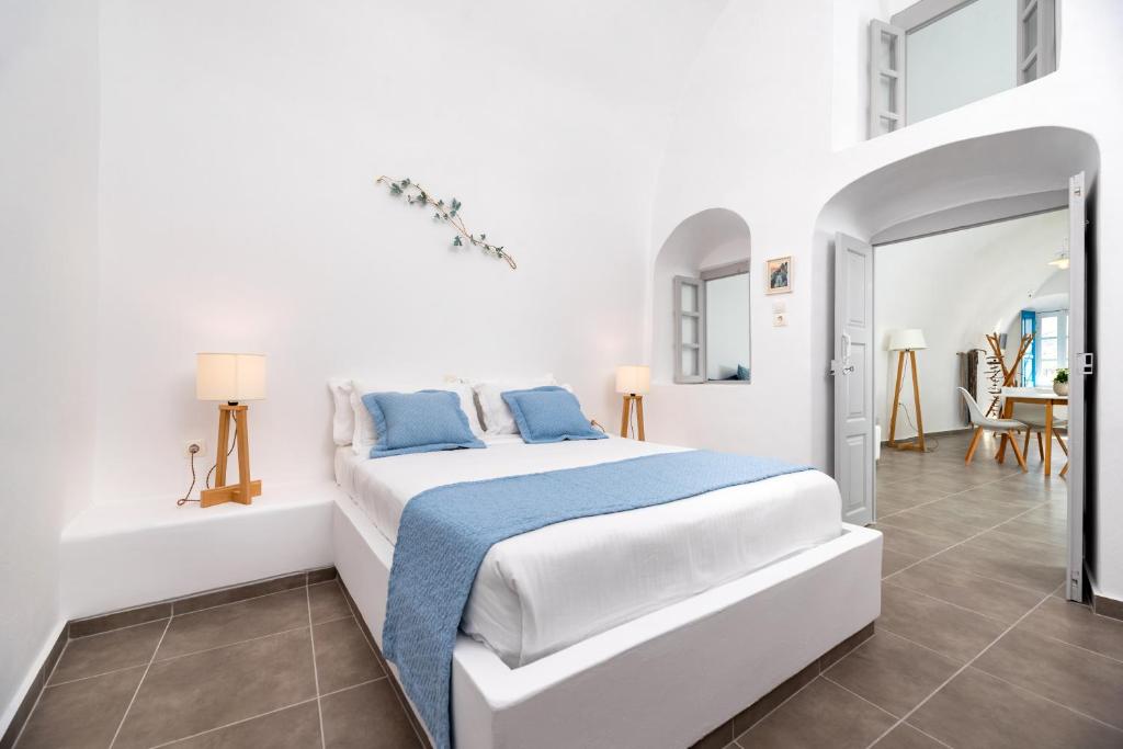 een witte slaapkamer met een bed met blauwe kussens bij Whitewashed Houses in Mesariá