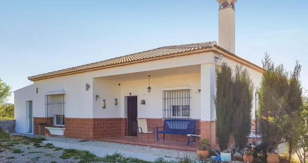 ein kleines weißes Haus mit einer blauen Bank davor in der Unterkunft Las Cormenillas in Olvera