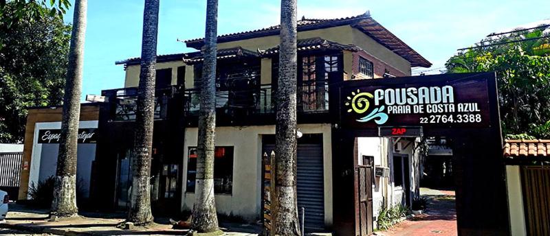 a building with a sign in front of it with palm trees at Pousada Suites Praia de Costazul in Rio das Ostras
